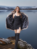 Woman in a black dress and knee-high boots standing on a rocky landscape with water in the background
