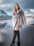 Woman in a fur coat standing in front of a mountainous landscape with water.