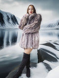 Woman in a fur coat standing in front of a snowy landscape with mountains and water.