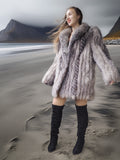 Woman wearing a fur coat and black boots on a beach with mountains in the background