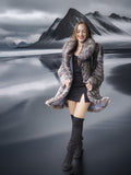 Woman in a fur coat standing in front of a mountainous landscape with a reflective lake.