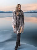 Woman in a fur coat and black boots standing in a reflective water landscape.