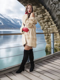 Woman in a fur coat and red gloves standing on a wooden deck with a scenic background