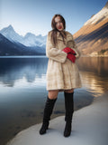Woman in a fur coat and red gloves standing by a lake with mountains in the background