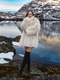 Model hugging Soft Plush Blush Fox Jacket S/M by a lake, showcasing the coat’s warmth and elegant white fox fur texture.