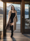 Woman in a long coat standing in front of a door with a mountain view.