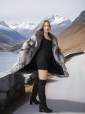 Woman in a fur coat and black dress standing in front of mountains and water