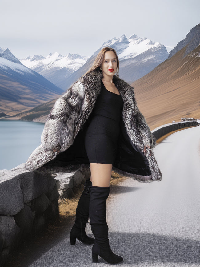 Woman in a fur coat and black dress standing in front of mountains and water