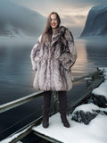 Woman in a fur coat standing on a snowy dock with a mountainous landscape in the background