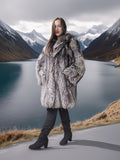 Person wearing a fur coat standing on a road with mountains and a lake in the background