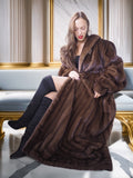 Woman wearing a long brown fur coat sitting on a decorative bench.