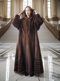 Woman in a long brown fur coat standing in an elegant interior setting.