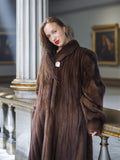 Woman wearing a long brown fur coat in an elegant interior setting.