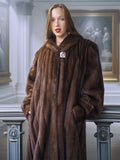 Woman wearing a long brown fur coat in an elegant interior setting.