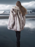 Person wearing a fur coat standing on a reflective surface with mountains in the background