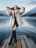 Woman in a fur coat and knee-high boots standing on a dock with a mountainous landscape in the background