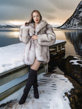 Woman in a fur coat standing on a snowy dock with mountains in the background