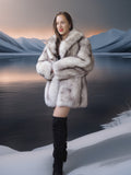 Woman in a fur coat standing in a snowy landscape with mountains in the background