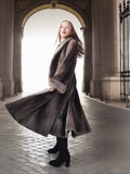 Woman in a long coat standing in an archway with a light background