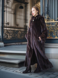 Woman in a long dark fur coat standing in front of an ornate door.