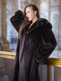 Woman wearing a dark fur coat standing indoors with a blurred background