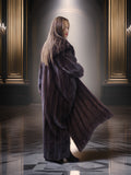 Woman in a long fur coat standing in an elegant room with chandeliers.