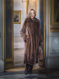Woman in a long brown fur coat standing in an elegant interior setting.