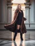 Woman in a long brown coat standing in an elegant interior setting