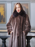 Woman wearing a long brown fur coat with a fur collar in an elegant interior setting.