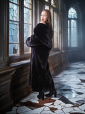 Woman in a long dark fur coat standing in a room with stained glass windows.