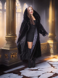 Woman in a long black fur coat standing in an ornate room with gold columns and marble floor.