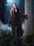 Woman in a long dark fur coat standing in a forest at night.