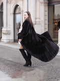 Luxurious NAFA black mink fur coat for women with a dramatic 94-inch sweep, styled with knee-high boots in an elegant city setting.