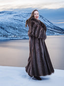 Smiling model in Silver Tip Canadian Raccoon Fur Coat by snowy lake. Luxurious fur outerwear for winter elegance.