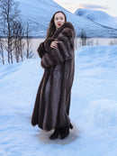 Model posing in Silver Tip Canadian Raccoon Fur Coat with snowy backdrop. Luxurious fur coat for winter elegance.