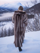 Rear view of Silver Tip Canadian Raccoon Fur Coat in snowy forest. Full-length luxury fur coat for cold weather.