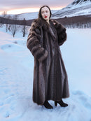 Model wearing Canadian Raccoon Fur Coat - Silver Tips M in snowy sunset. Full-length fur coat for elegant winter style.