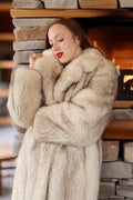 Woman wearing a fur coat in front of stacked stone bricks.