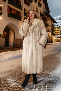 Woman in a fur coat standing on a snowy street with mountains in the background