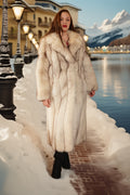 Woman in a fur coat standing on a snowy path with mountains in the background