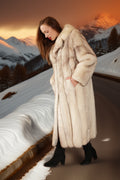 Woman in a fur coat standing in front of a snowy mountain landscape