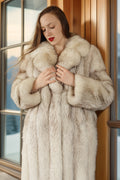Woman wearing a fur coat standing indoors with a window in the background