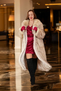 Woman in a long fur coat and red dress walking in an indoor setting.