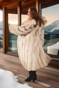 Woman in a fur coat standing on a wooden deck with a mountain view.