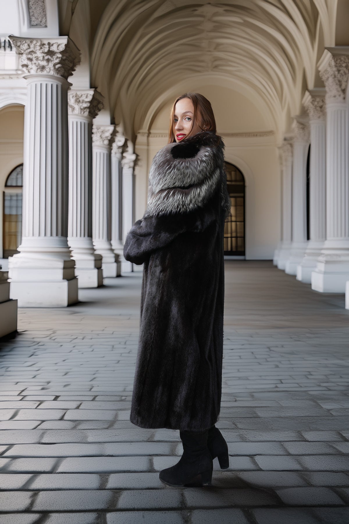 A woman wearing a long dark fur coat with a gray and white fur collar stands in a grand arched corridor with columns.
