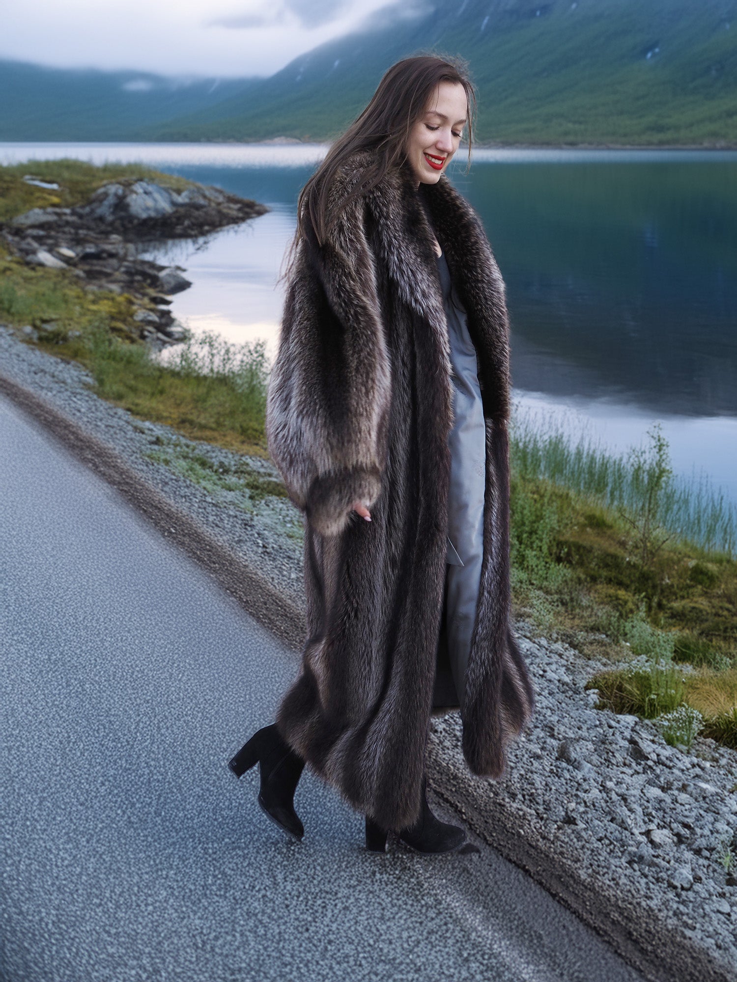Woman walking in Canadian Raccoon Fur Coat along lakeside road, highlighting natural fur sheen and elegant cold-weather style.