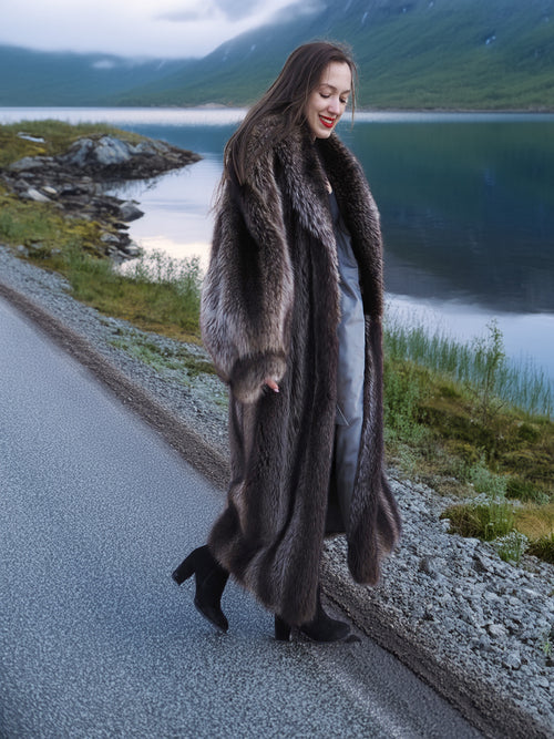 Woman walking in Canadian Raccoon Fur Coat along lakeside road, highlighting natural fur sheen and elegant cold-weather style.