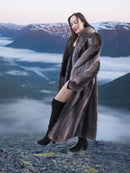 Model in raccoon fur coat standing on cliff with cloud-covered valley, showcasing premium natural fur outerwear for winter.