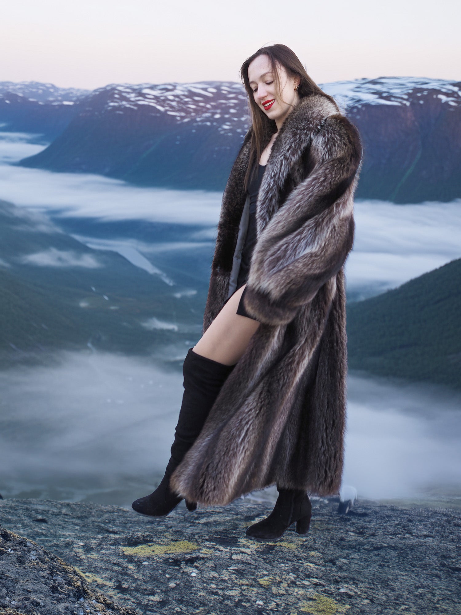 Model in raccoon fur coat standing on cliff with cloud-covered valley, showcasing premium natural fur outerwear for winter.