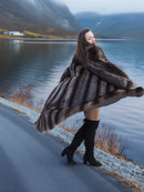 Luxury full-length raccoon fur coat in natural tones, modeled by lake with mountain backdrop, stylish warm outerwear for winter.